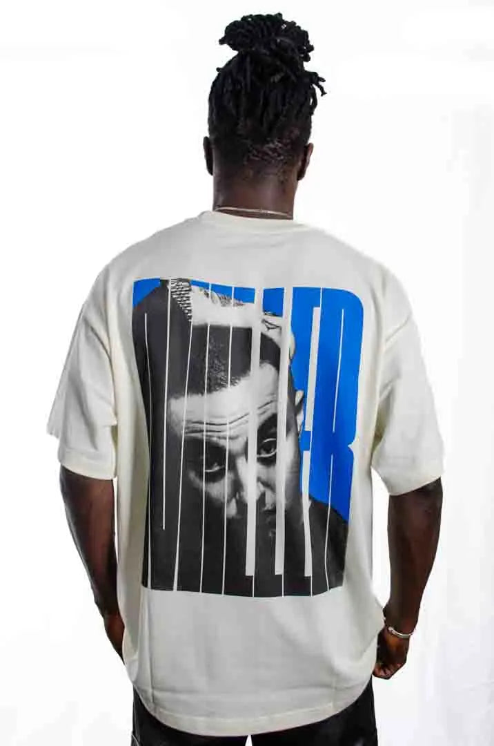 Vista trasera de un modelo hombre vistiendo la Camiseta Mac Miller. Camiseta streetwear oversized con hombros caídos. Algodón 100% orgánico en color Leche de coco.