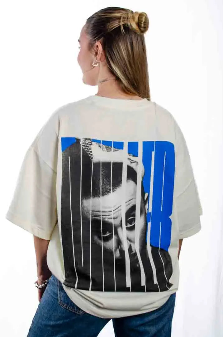 Vista trasera de una modelo mujer vistiendo la Camiseta Mac Miller. Camiseta streetwear oversized con hombros caídos. Algodón 100% orgánico en color Leche de coco.