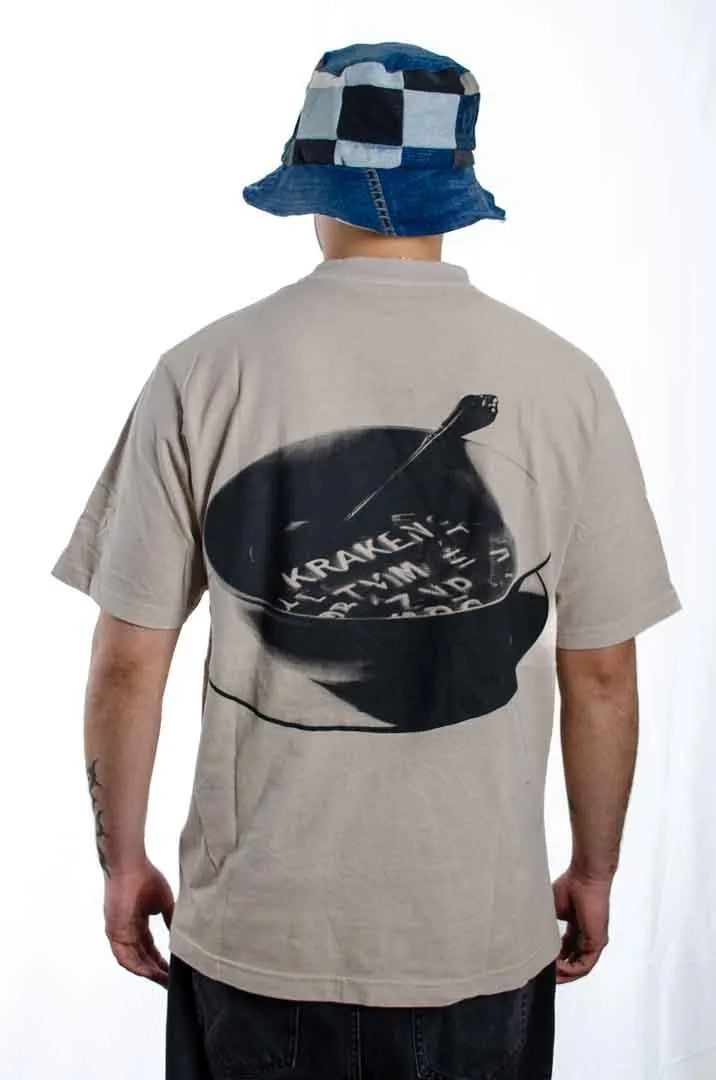 Vista trasera de un modelo hombre vistiendo la Camiseta Sancocho. Camiseta streetwear oversized efecto lavado en color gris ciudad, confeccionada en 100% algodón orgánico.