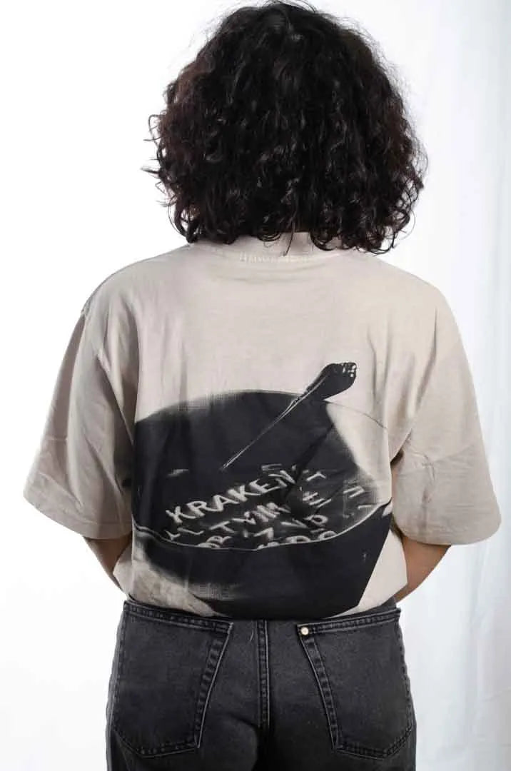 Vista trasera de una modelo mujer vistiendo la Camiseta Sancocho. Camiseta streetwear oversized efecto lavado en color gris ciudad, confeccionada en 100% algodón orgánico.