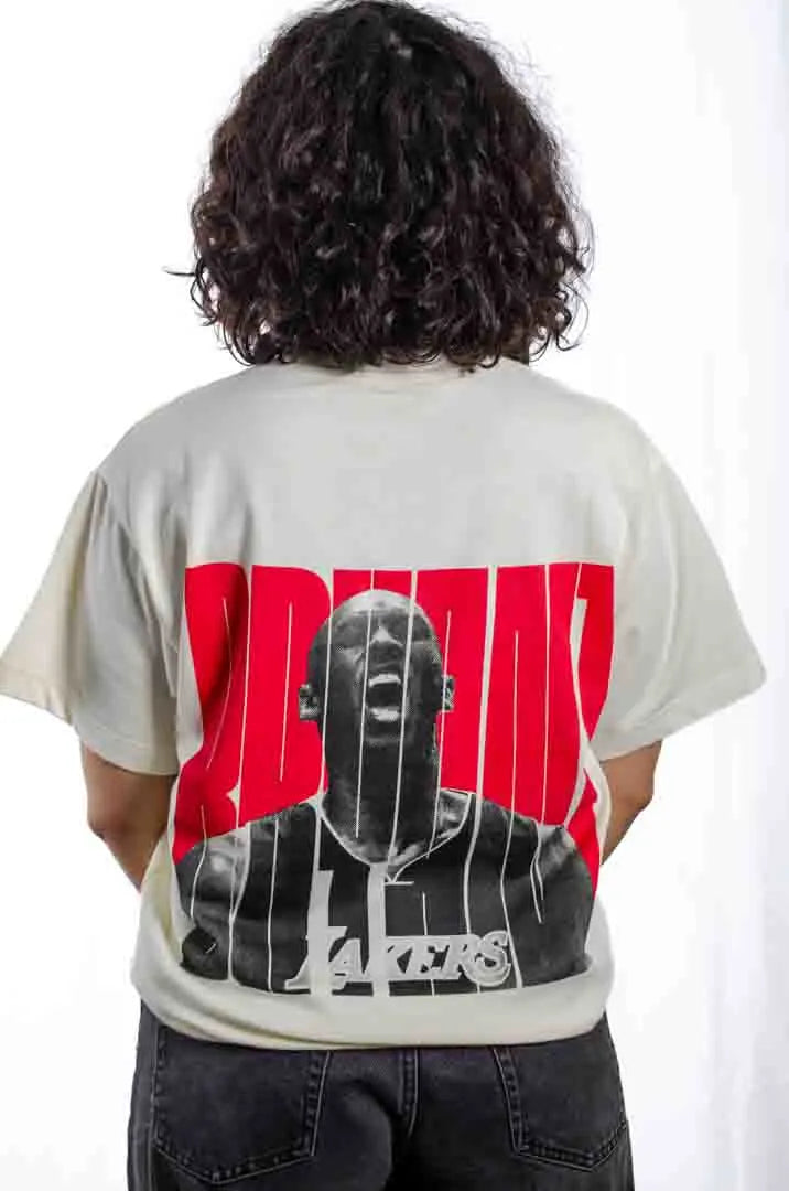 Vista trasera de una modelo mujer vistiendo la Camiseta Kobe Bryant. Camiseta streetwear oversized con hombros caídos, de algodón 100% orgánico en color Leche de coco.