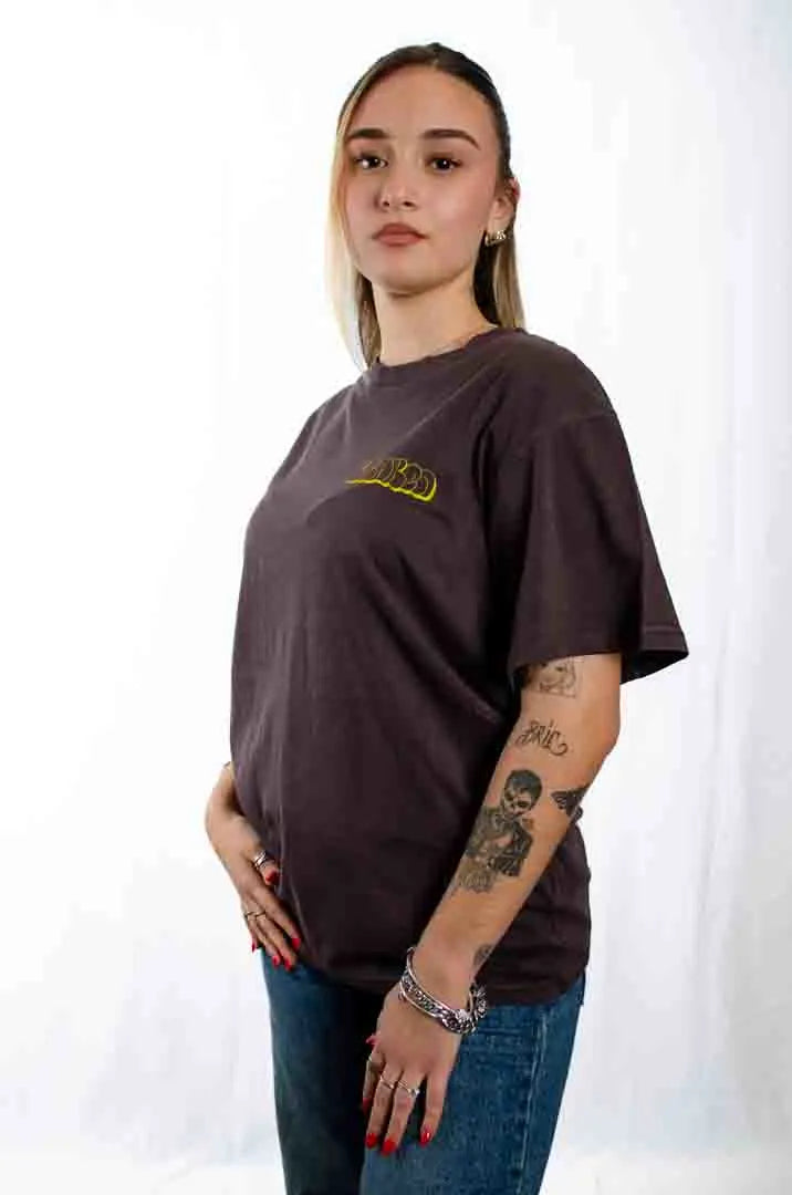 Vista lateral de una modelo mujer vistiendo la Camiseta La True Face. Camiseta streetwear oversized efecto lavado en color café americano, de algodón orgánico.