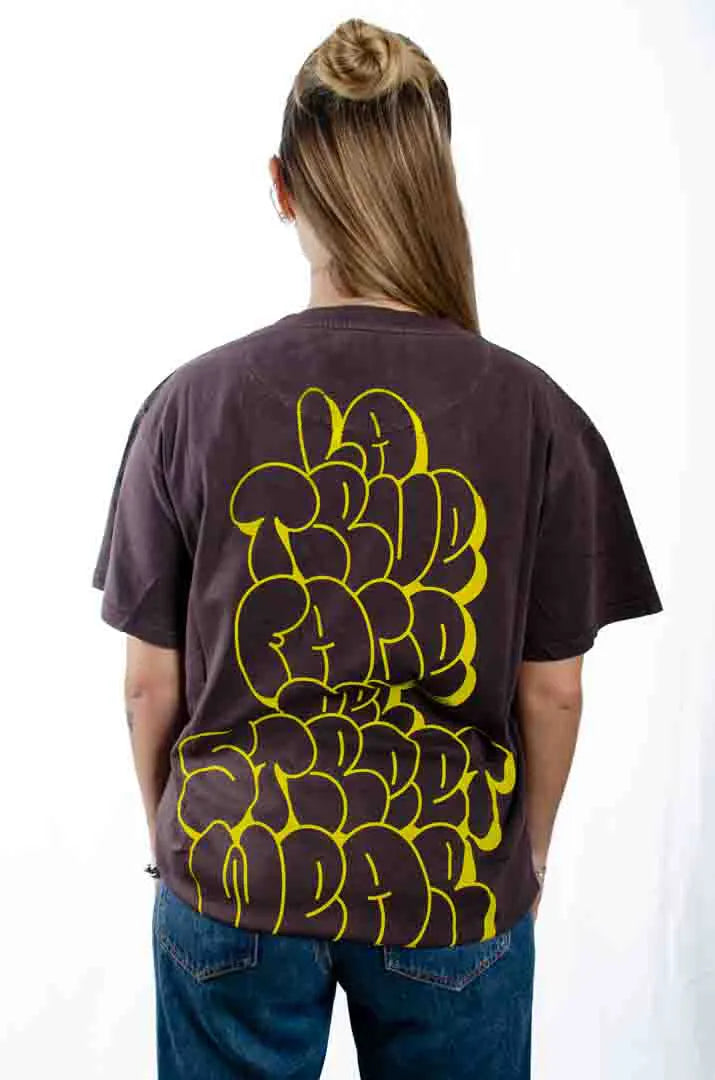 Vista trasera de una modelo mujer vistiendo la Camiseta La True Face. Camiseta streetwear oversized efecto lavado en color café americano, de algodón orgánico.