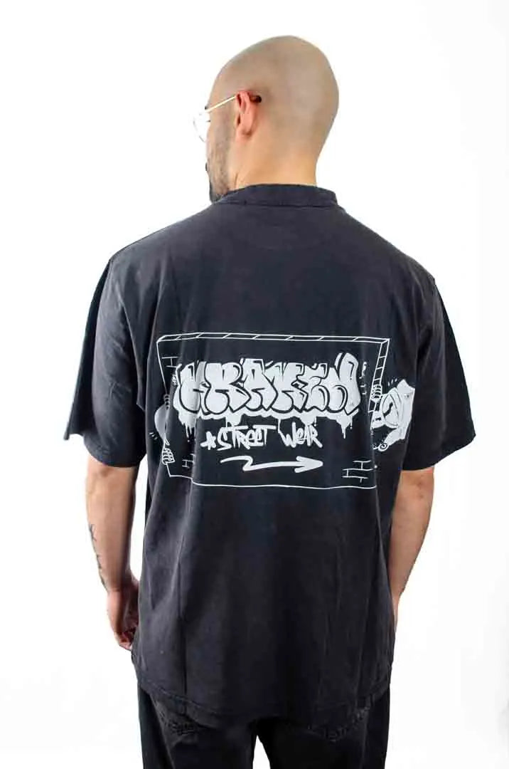 Vista trasera de un modelo hombre vistiendo la Camiseta Tu tío Paco. Camiseta streetwear oversized efecto lavado en color negro, hecha con algodón 100% orgánico