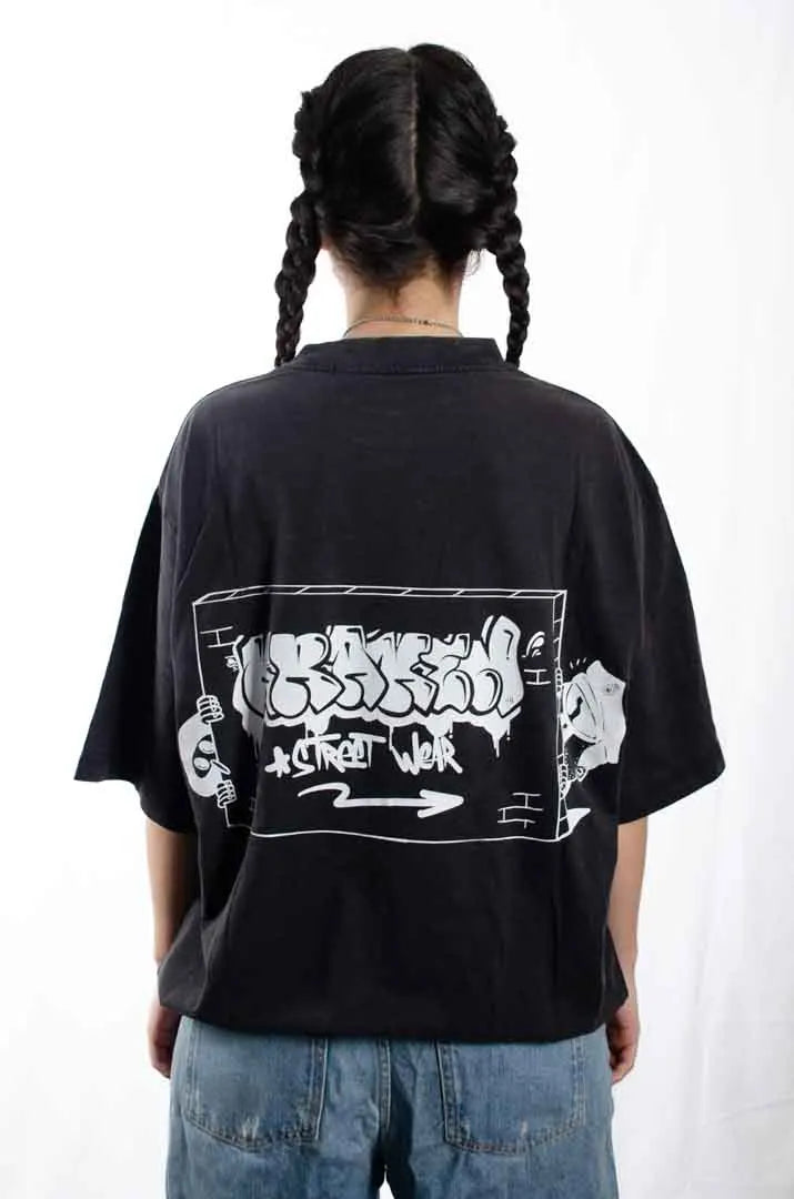 Vista trasera de una modelo mujer vistiendo la Camiseta Tu tío Paco. Camiseta streetwear oversized efecto lavado en color negro, hecha con algodón 100% orgánico.