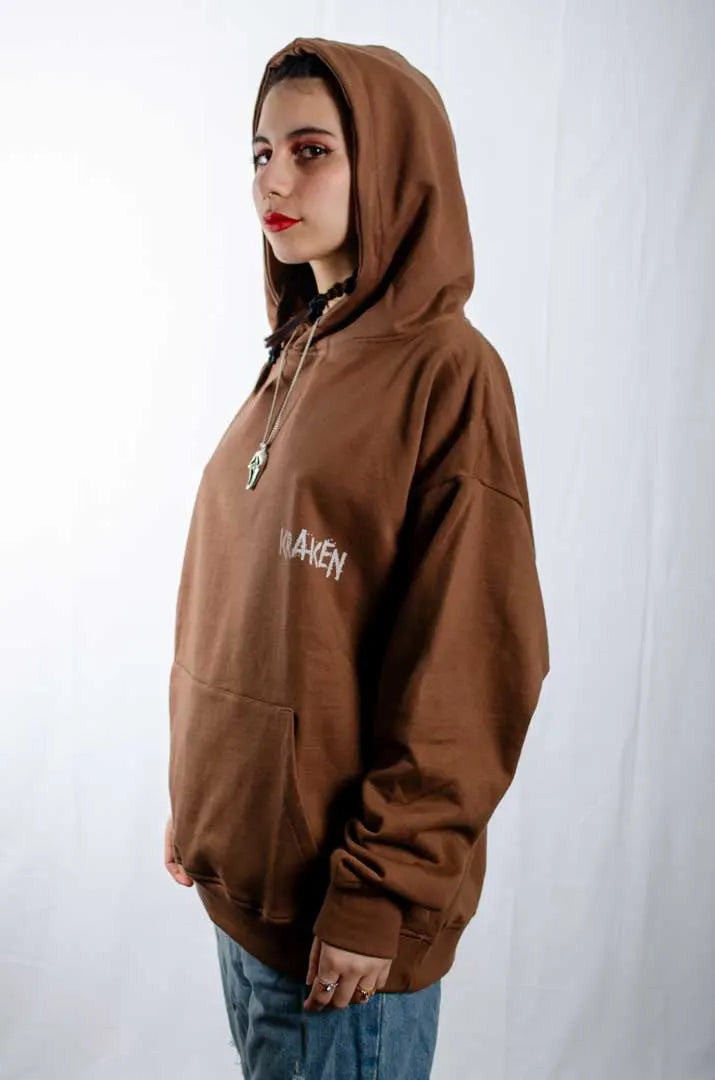 Vista lateral de una modelo mujer vistiendo la Sudadera El Orgullo de tu Papá. Sudadera streetwear oversized con capucha, en color Brownie especial y fabricada con material de felpa perchada 100% algodón.