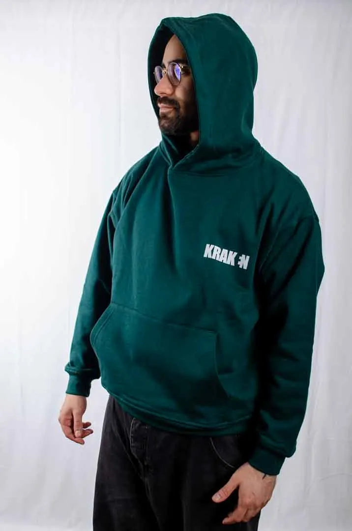 Vista lateral de un modelo hombre vistiendo la Sudadera Keloke. Sudadera streetwear oversized con capucha, en color verde solera y fabricada con material de felpa perchada 100% algodón.