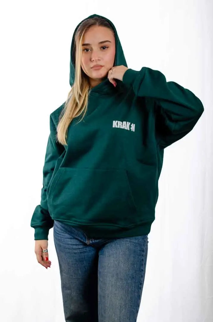 Vista frontal de una modelo mujer vistiendo la Sudadera Keloke con capucha puesta. Sudadera streetwear oversized, en color verde solera y fabricada con material de felpa perchada 100% algodón.