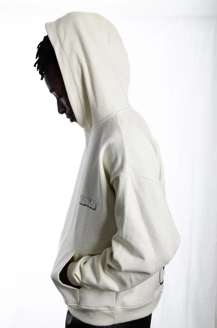 Vista lateral de un modelo hombre vistiendo la Sudadera La True Face. Sudadera hoodie oversized con capucha, 100% algodón felpa en color Leche de coco.